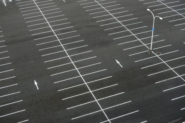 Overhead view of a striped asphalt parking lot with marked spaces and directional arrows